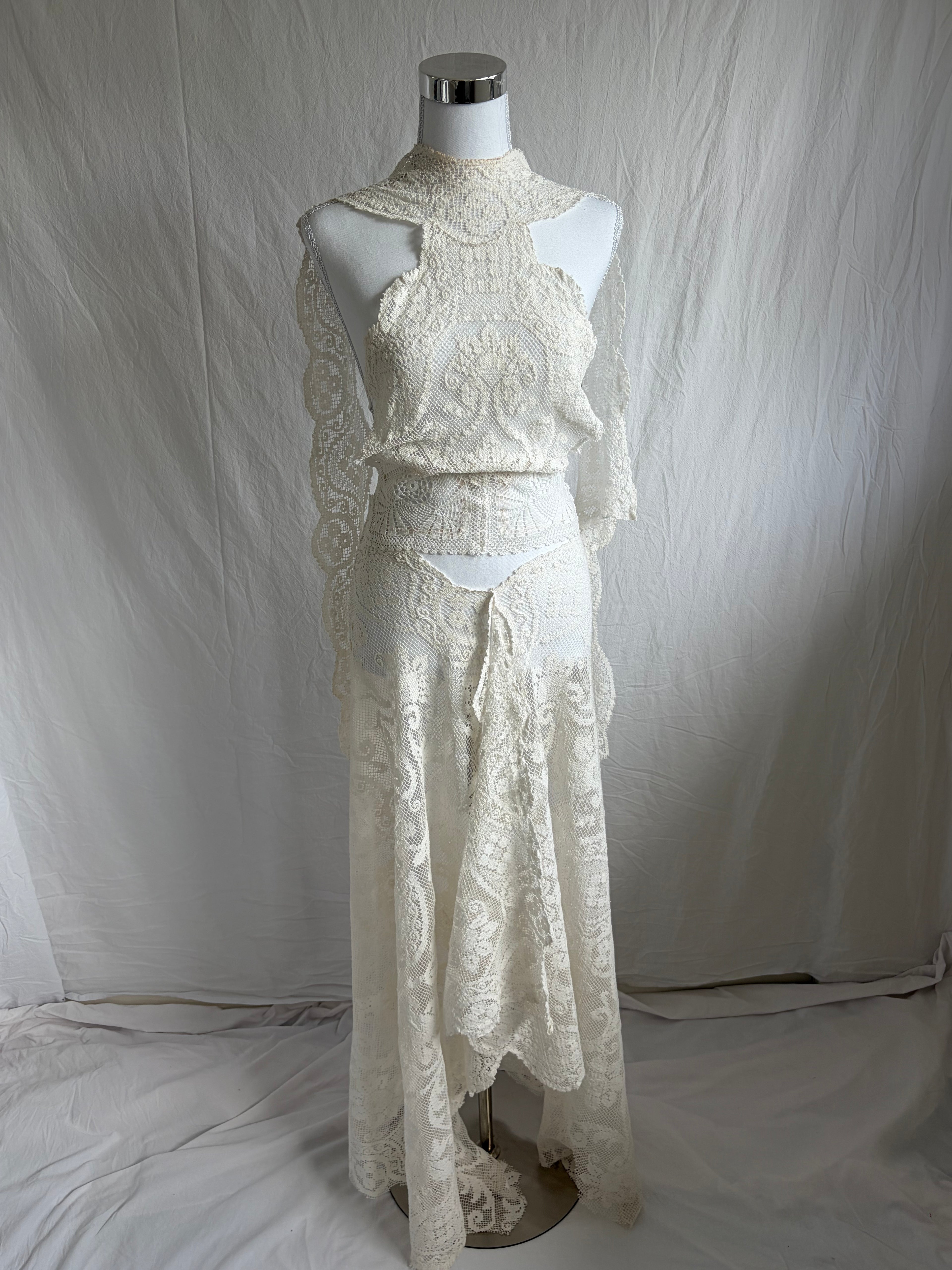 Ivory or cream lace two-piece set with long sleeves. The top features a high mock neck, an open shoulder/keyhole cutout design, and flared lace sleeves. The skirt is a matching high-waisted, asymmetrical maxi length with a handkerchief hem.