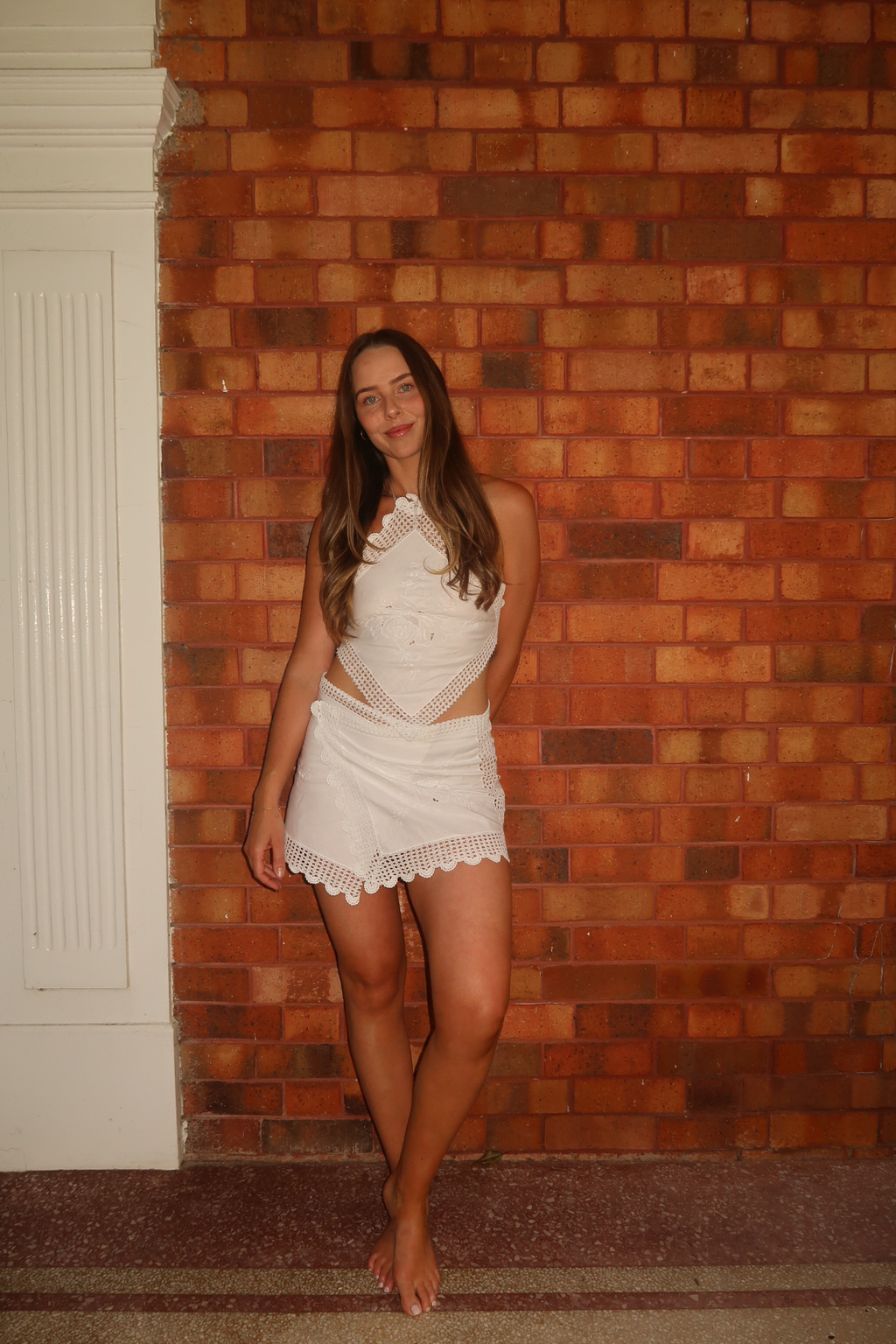 White upcycled two-piece set featuring vintage embroidered handkerchiefs. The set includes a diamond-shaped halter-neck top with scalloped crochet lace edges and a mini wrap skirt with a matching scalloped lace hem.