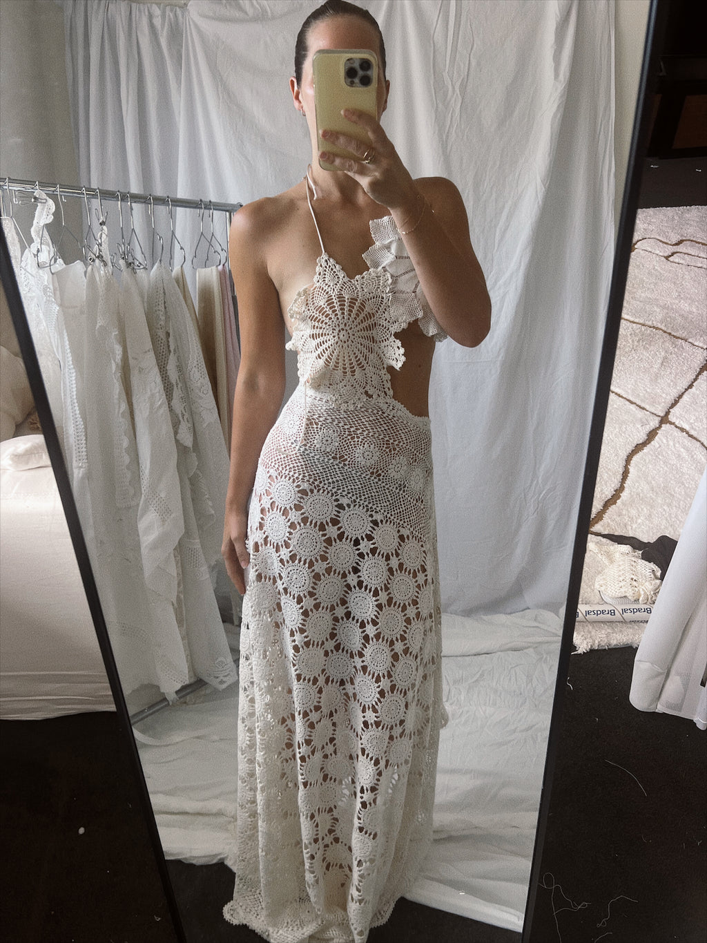 Vintage-style cream crochet two-piece set. The set includes a cropped halter top adorned with oversized three-dimensional floral appliqué details, and a high-waisted, asymmetrical maxi skirt featuring large circular crochet floral patterns.
